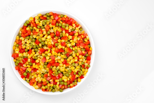 a mix of chopped vegetables paprika, corn, peas in white plate top view