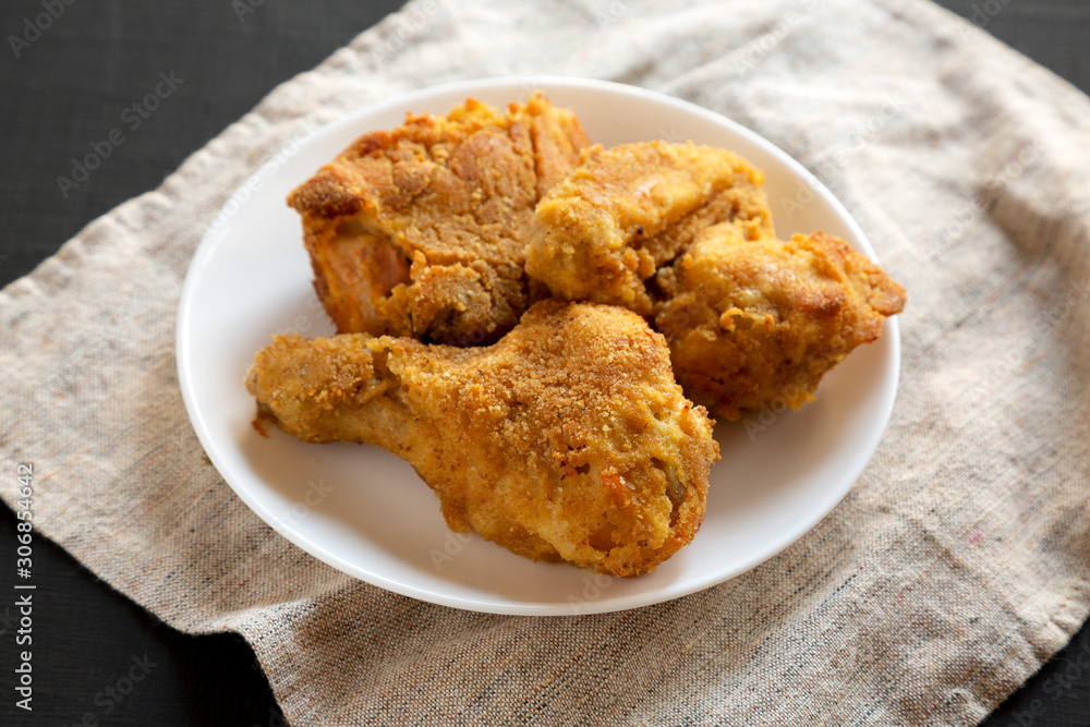 Delicious homemade oven baked fried chicken on a white plate over black background, low angle view. Close-up. Delicious homemade oven baked fried chicken on a white plate over black background, low angle view. Close-up.