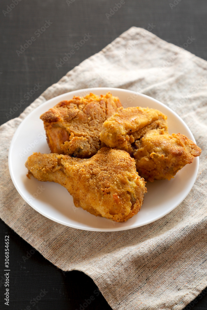 Delicious homemade oven baked fried chicken on a white plate over black surface, low angle view. Close-up. Delicious homemade oven baked fried chicken on a white plate over black surface, low angle view. Close-up.