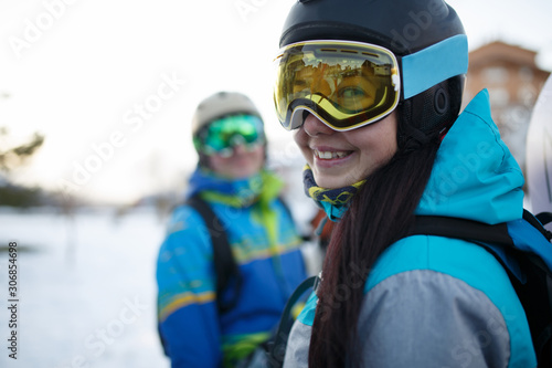 Photo of smiling woman in mask with snowboard and men at snow resort.