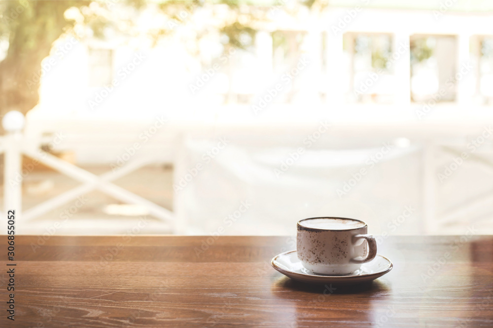 Rustic cup of cappuccino with saucer on a wooden table of a coffee shop by the window with bright sunlight. Copy space. Rustic cup of cappuccino with saucer on a wooden table of a coffee shop by the window with bright sunlight. Copy space.