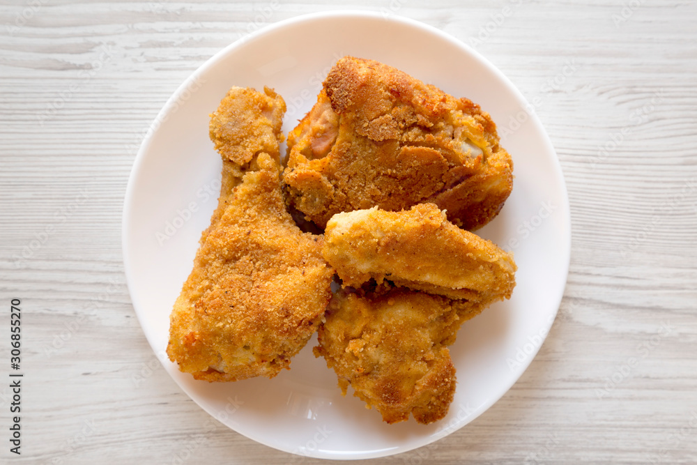 Delicious homemade oven baked fried chicken on a white plate on a white wooden surface, top view. Overhead, from above, flat lay. Close-up. Delicious homemade oven baked fried chicken on a white plate on a white wooden surface, top view. Overhead, from above, flat lay. Close-up.