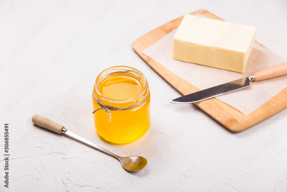 Ghee or clarified butter in a glass jar on a neutral textured background next to a spoon. Ghee or clarified butter in a glass jar on a neutral textured background next to a spoon.