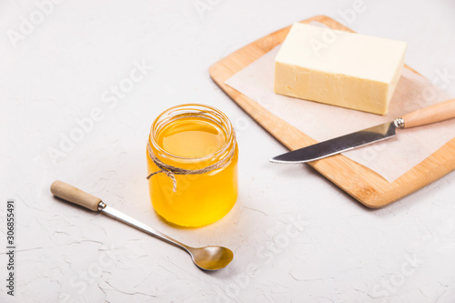 Ghee or clarified butter in a glass jar on a neutral textured background next to a spoon.