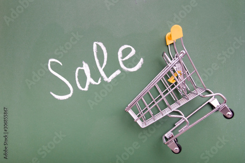 Shopping trolley and inscription sale on green chalk board, copy space top view.