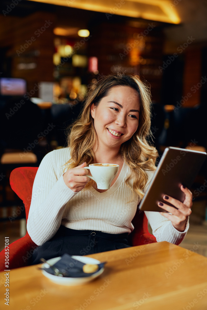 Beautiful Asian woman drinking coffee and looking at her tablet Beautiful Asian woman drinking coffee and looking at her tablet