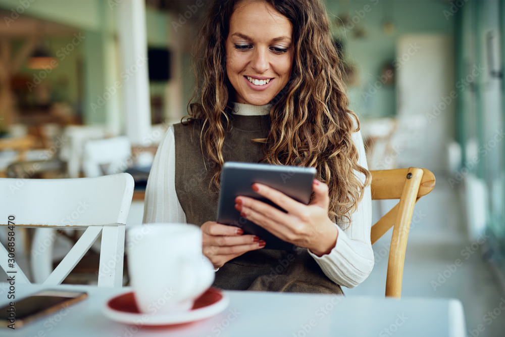 Attractive young curly brunette enjoying her coffee/tea and working on tablet Attractive young curly brunette enjoying her coffee/tea and working on tablet