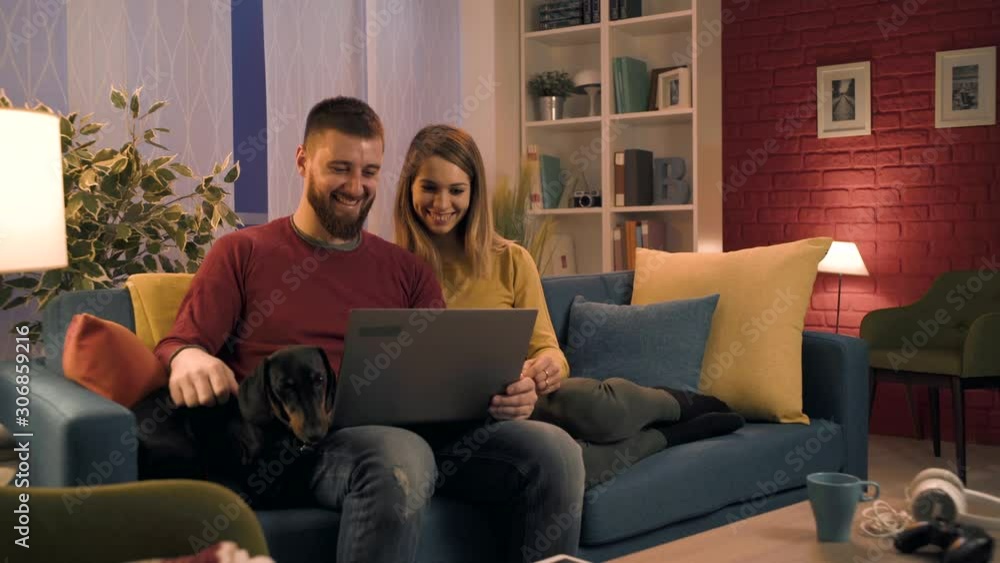 Happy couple sitting on the sofa and connecting with their laptop Happy couple sitting on the sofa and connecting with their laptop