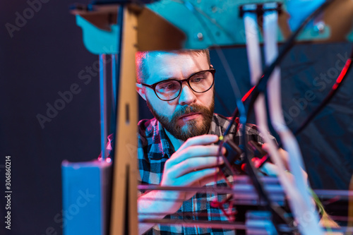 Young male designer engineer using a 3D printer in the laboratory and studying a product prototype, technology and innovation concept
