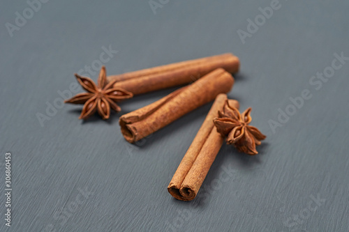 Three flavour cinnamon sticks near stars of anise lies on dark scratched desk on kitchen. Close-up