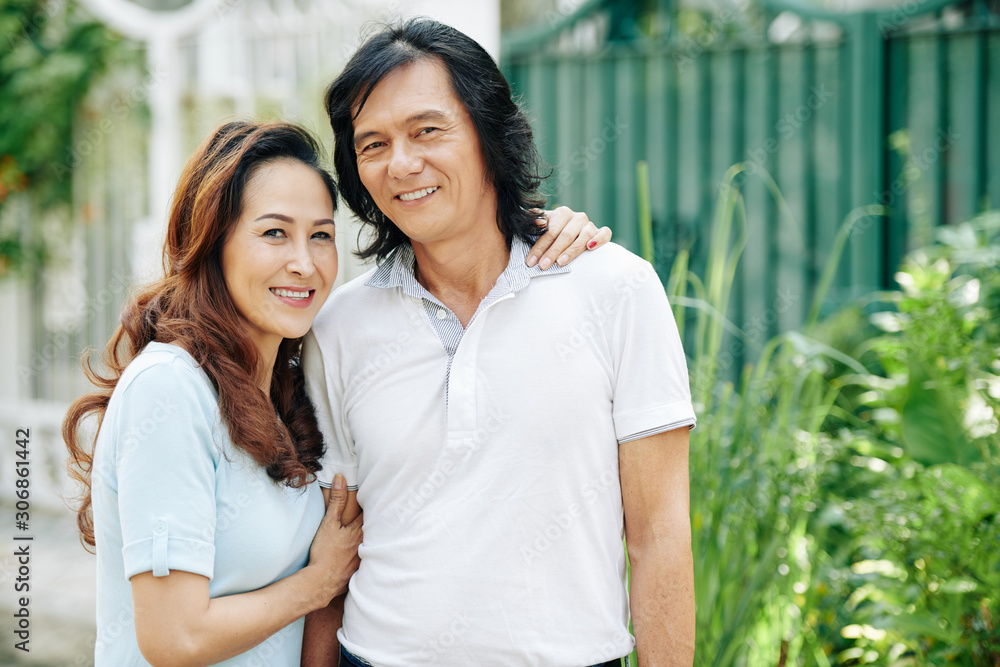 Positive Asian middle-aged couple hugging and posing in the street together Positive Asian middle-aged couple hugging and posing in the street together