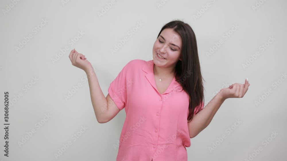 Cheerful young woman keeping fists up, smiling isolated on gray background in studio in casual pink shirt. People sincere emotions, lifestyle concept. Cheerful young woman keeping fists up, smiling isolated on gray background in studio in casual pink shirt. People sincere emotions, lifestyle concept.