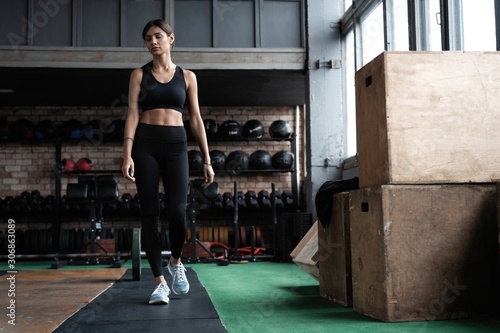 Shot of strong woman standing in crossfit gym and looking away. Confident fitness female model in sportswear.