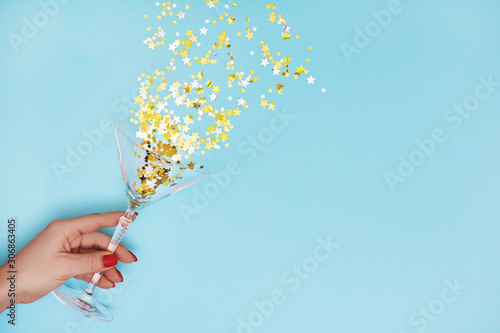 Fotografija Woman hand holding martini glass with pouring out golden stars confetti on blue background