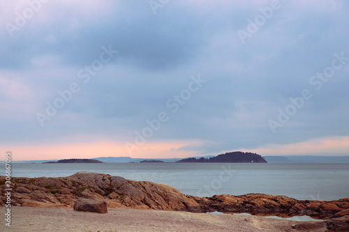 Landscape of Oslo Fjord with small islands, calm water, overcast sky. orange rocks on the beach, tranquility. Pastel colors. Norwegian coastline in summer. Nesodden Norway. Nesoddtangen peninsula.