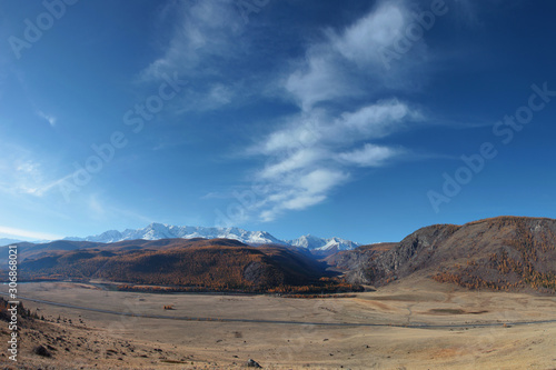 Mountain landscape. Spacious valley, snowy ridge and blue sky with white clouds.