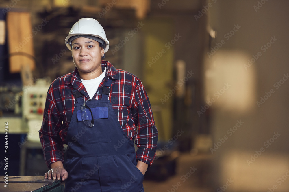 Waist up portrait of modern female worker looking at camera while leaning on machine units in industrial plant, copy space