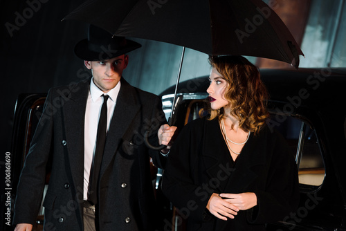 handsome man in hat holding umbrella near attractive girl and vintage car © LIGHTFIELD STUDIOS