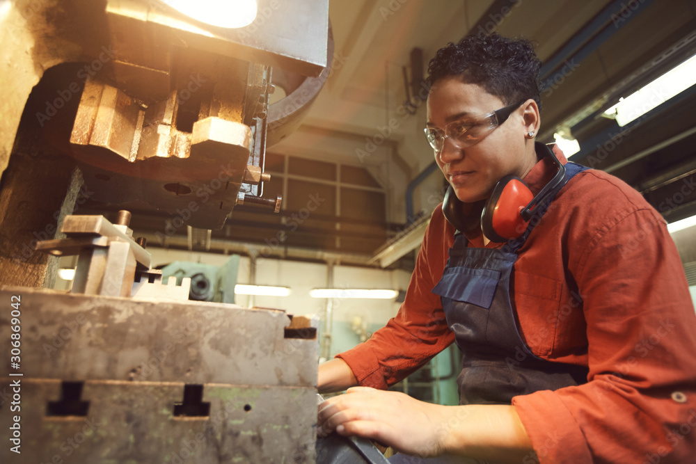 Side view portrait of smiling woman operating industrial machine units at metalworking plant, copy space