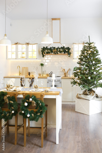 Christmas decor. Bright interior of white kitchen with decorated Christmas tree, garlands and Christmas wreaths.