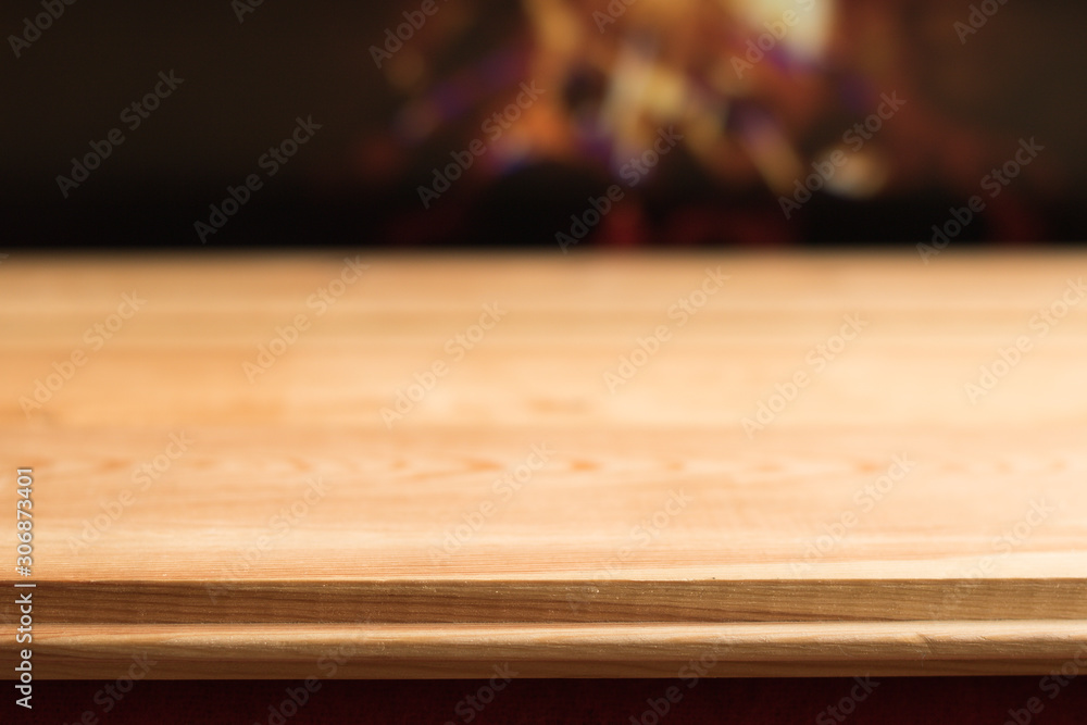 Close-up: Simple Wooden Table with Empty Space against Blurred Bright Burning Fire in Fireplace – Background, Banner, Copy Space. 