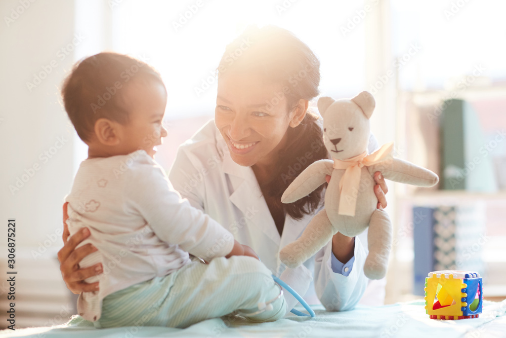 Young female doctor smiling and playing with baby boy during her visit - obrazy, fototapety, plakaty 