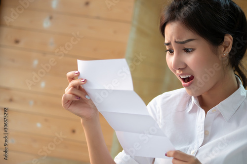 frustrated, shocked, stress women screaming at expensive bill or debt notice invoice; concept of high cost of living, expensive bill, no money, getting bused; asian young adult woman model photo
