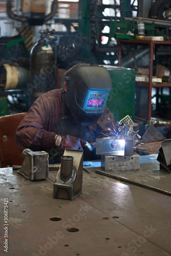 worker in mask, in the process of welding metal with bright light, smoke and sparks