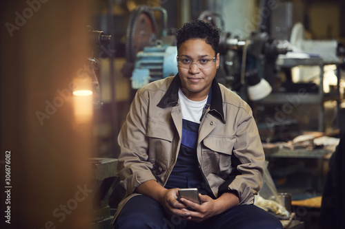 Portrait of contemporary mixed-race woman smiling at camera while posing in factory workshop