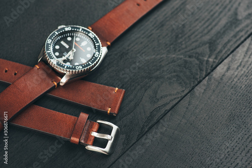 Men's luxury watch with brown leather handmade watch strap laying on the black wooden surface. Copy space for the text.