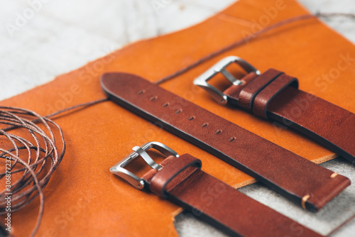 Closeup leather handmade watch strap with steel buckle no orange leather laying on wooden rustic surface next to special tools and leather thread. Copy space.