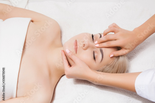 Concept of therapeutic anti-aging skin tightening facial treatments. Close-up hands of an unidentified young woman masseur doing facial massage to beautiful young caucasian client woman at spa salon.