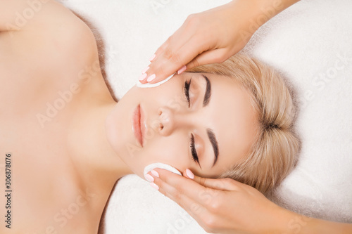Doctor beautician cleanses face skin with sponge in beauty salon. Perfect cleaning healthcare spa treatment. Skincare beauty spa concept. Model lying on couch with closed eyes in cosmetological clinic