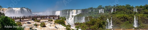Obraz na plátně Panorama of spectacular Iguazu Falls with visitor platform and blue sky