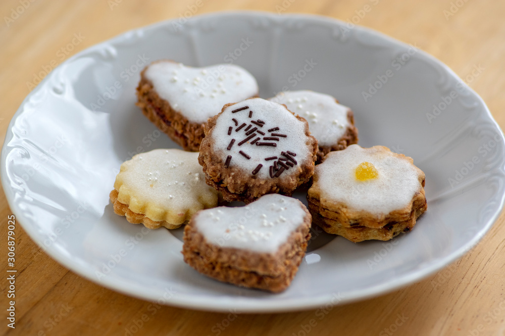 Jam and cream filled cookies with sugar sweet white icing on white plate on wooden table, group of Christmas sweets Jam and cream filled cookies with sugar sweet white icing on white plate on wooden table, group of Christmas sweets