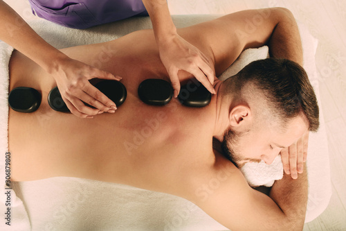 Handsome man at spa resort receive hot stone massage. Speciality massage using smooth, heated stones photo