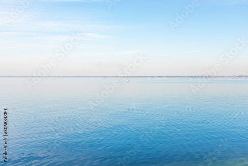 Calm landscape of sea water with fisher man in boat and a coast on horizon