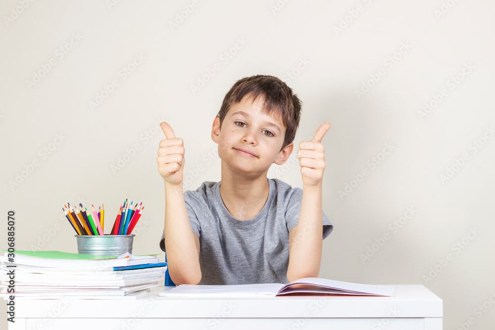 Happy boy making homework tasks and showing thumbs up sign Happy boy making homework tasks and showing thumbs up sign