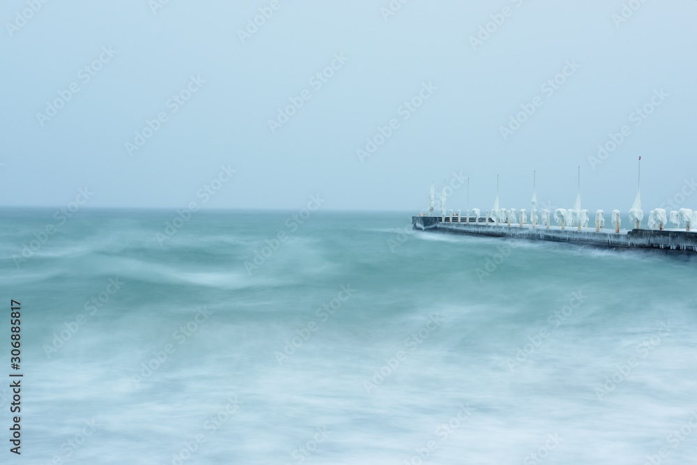 Winter sea landscape. Long exposure. The icy sea and the pier in ice, frozen icicles.