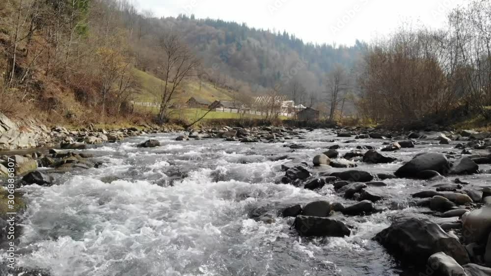Shooting from a drone along a mountain river running over stones towards a village in the Carpathians. Shooting from a drone along a mountain river running over stones towards a village in the Carpathians.