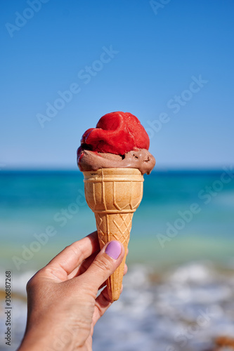 Waffle cup with ice cream in a female hand on a background of the sea