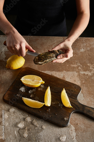 cropped view of woman holding knife while opening oyster near lemons
