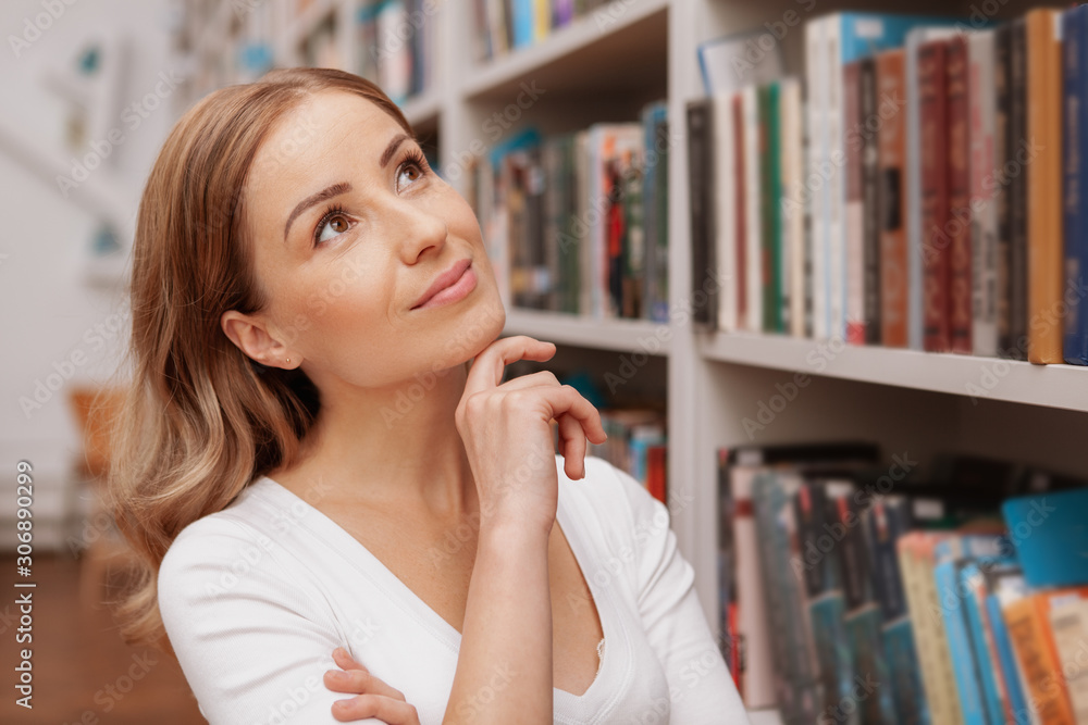 Close up of a beautiful cheerful woman smiling, looking at the bookshelves at the bookstore or library Close up of a beautiful cheerful woman smiling, looking at the bookshelves at the bookstore or library