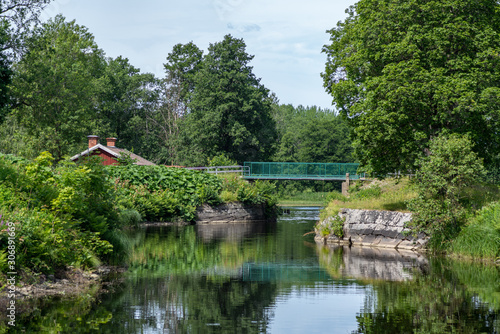 Fototapeta Naklejka Na Ścianę i Meble -  Beautiful canal with lush green vegetation in summer sunlight