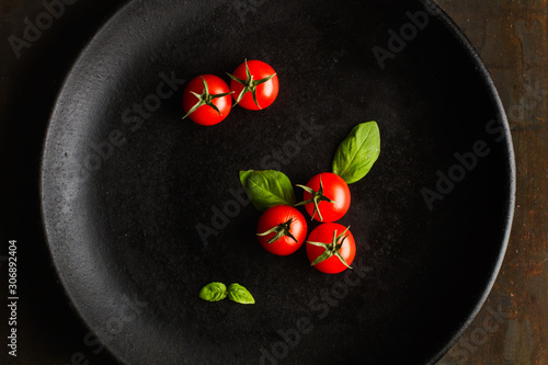 Tomates jitomate cherry naturales frescos con albahaca sobre plato negro redondo. Vista superior