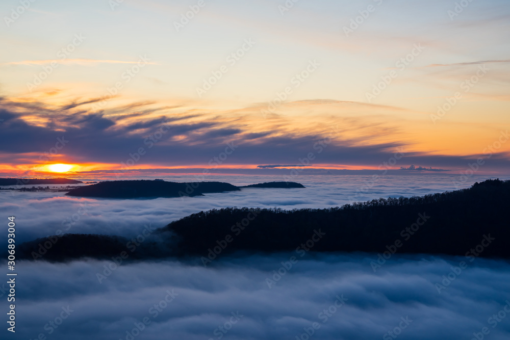 Germany, Magical aerial view above endless lake of fog clouds in valley of swabian alb nature landscape at sunset with orange sky near stuttgart on mountain breitenstein