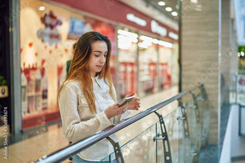 young woman in a shopping center stands near the fence and using app on the phone
