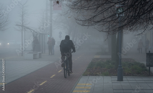 Cyclist in the city is moving along a bicycle path in fog