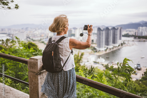 Traveler elderly backpacker woman taking photos overlooking the downtown. Travel adventure in China, Tourist beautiful destination Asia, Summer holiday vacation trip. Freedom and happy people concept