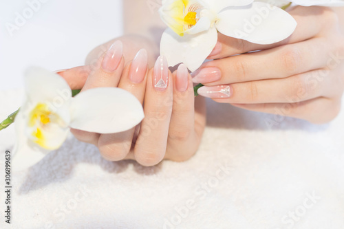 Beautiful soft woman hands with light manicure hand care and spa relaxing white orchid